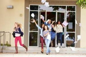 Šťastní studenti vycházejí ze školy a hážou papíry nad hlavu